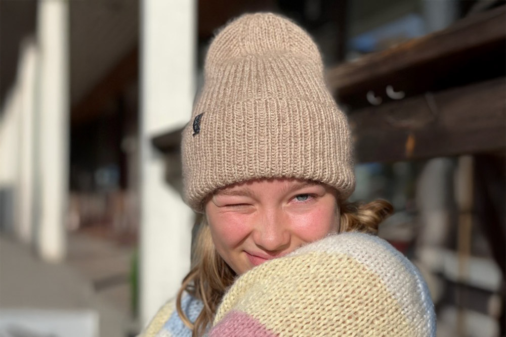 Närbild på en person som blinkar med ena ögat och bär en ljusbeige ribbstickad mössa samt en randig stickad tröja i pastellfärger.