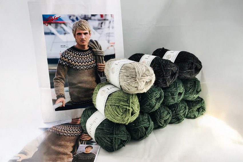 Garnpaket för en isländsk tröja (lopapeysa) i bruna, gråa och gröna nyanser. Flera nystan av Léttlopi ligger framför ett mönsterhäfte med en bild på en man i en stickad tröja.