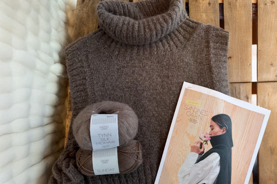 Garnpaket för en brun, högpolokrage väst. Två nystan Sandnes Garn Tynn Silk Mohair och Sunday ligger intill den stickade västen och ett mönsterhäfte.